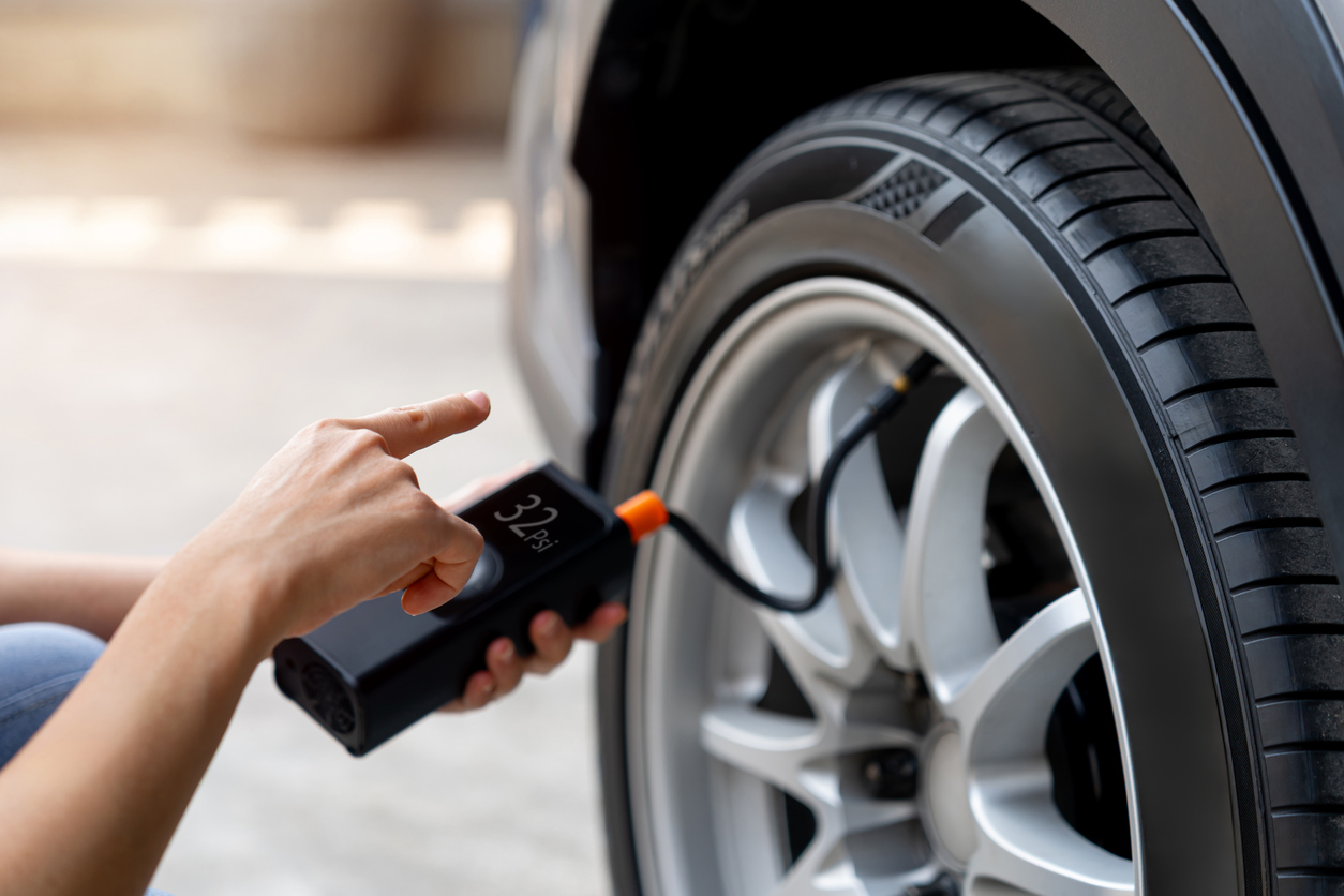close up of woman’s hand adjusting portable tire inflator to check air pressure before road trip