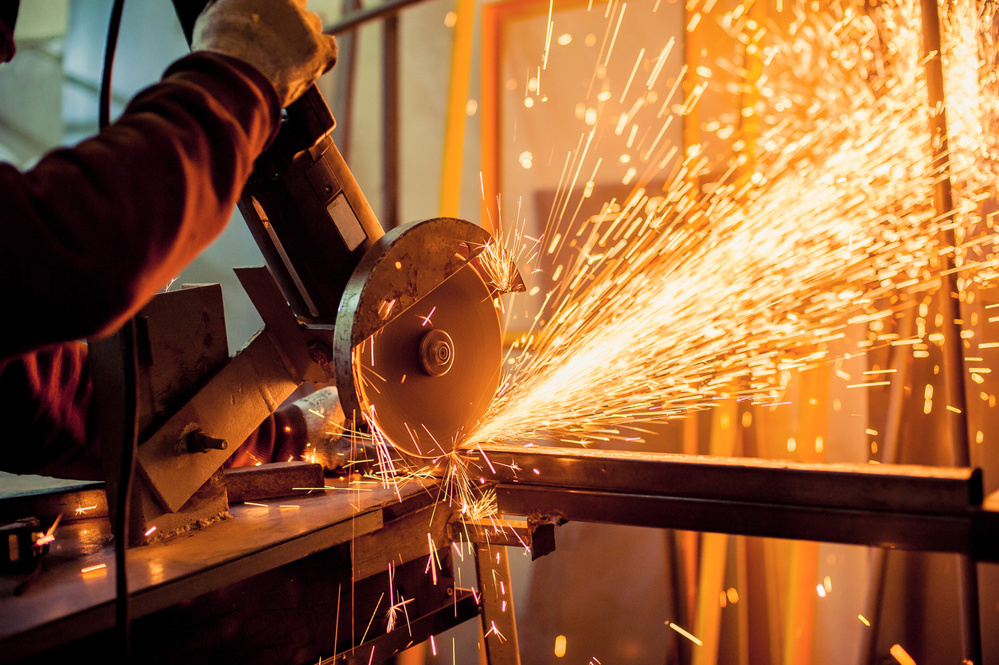 A man working with electric grinder tool on steel structure in factory, sparks flying